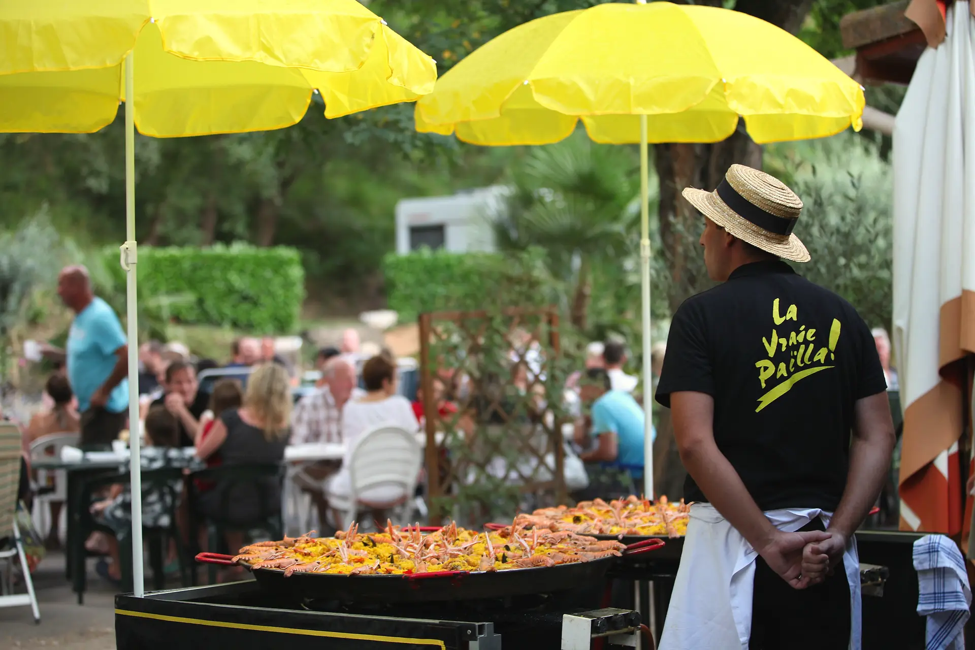Paella-Abend: der Koch an den großen Pfannen, die Urlauber an ihren Tischen unter gelben Sonnenschirmen