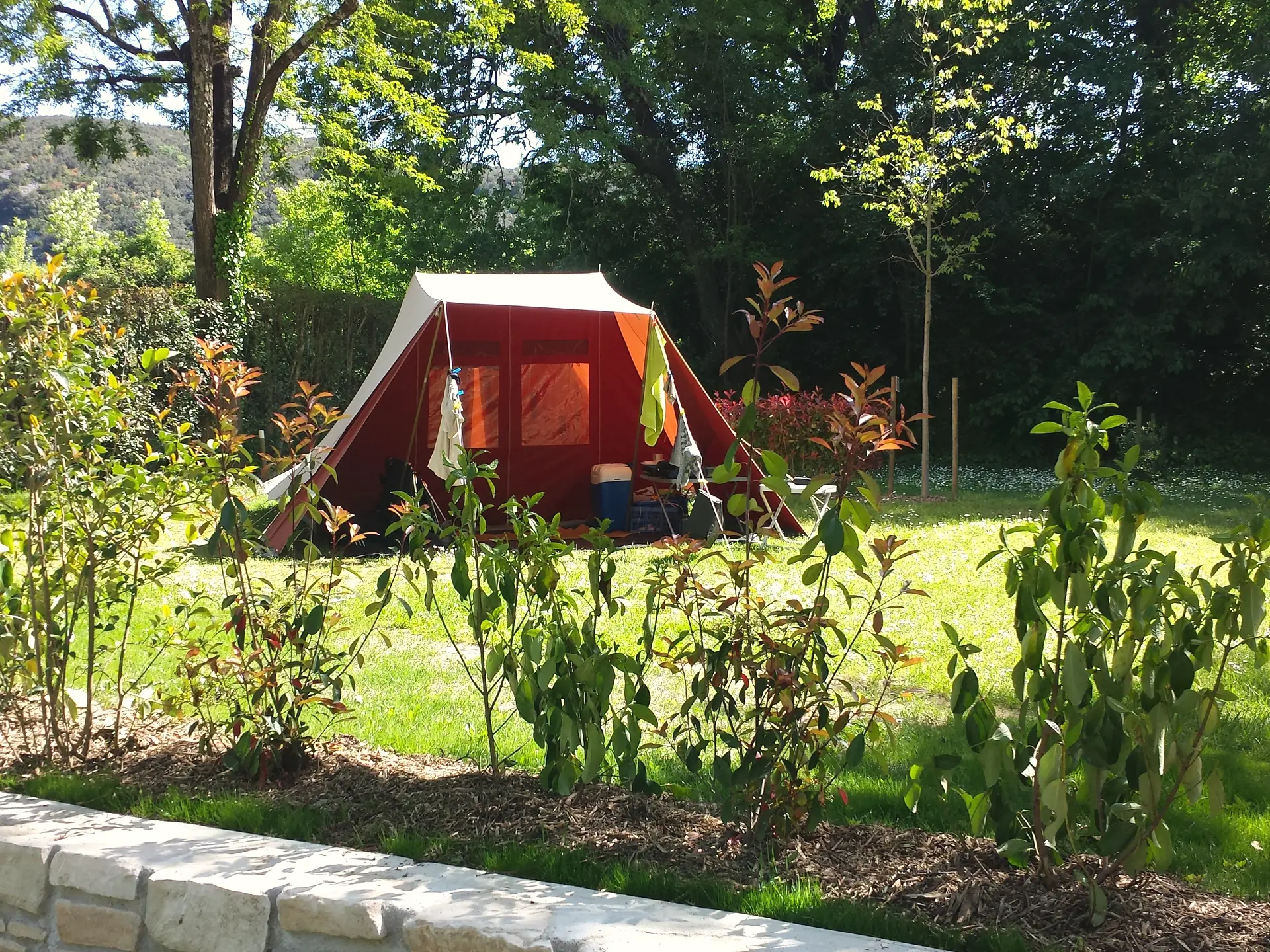 Ein Zelt auf einem Rasenstellplatz, zwischen Blumenbeeten und Bäumen