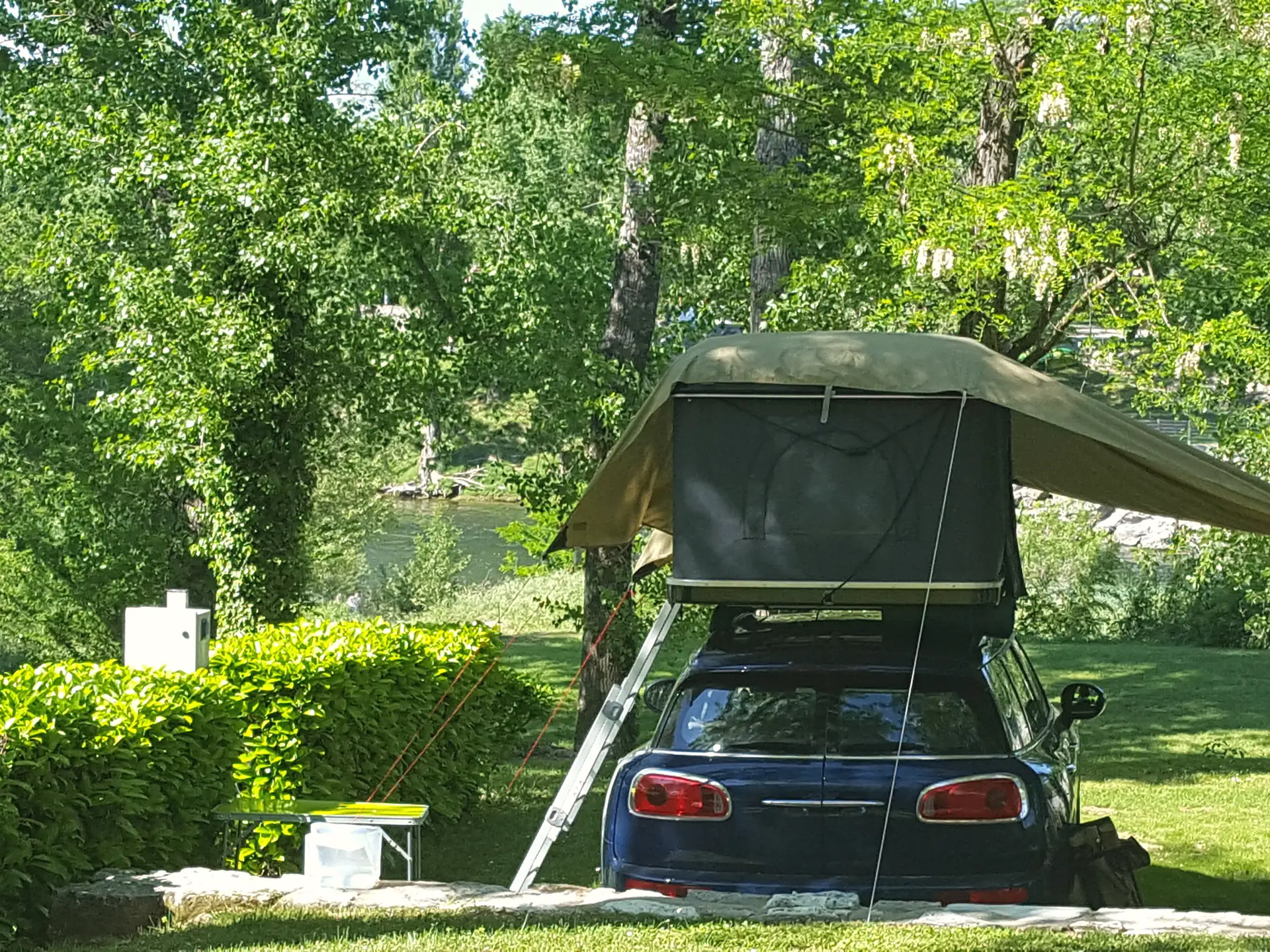 A car with a roof tent on a pitch, the river behind the hedge