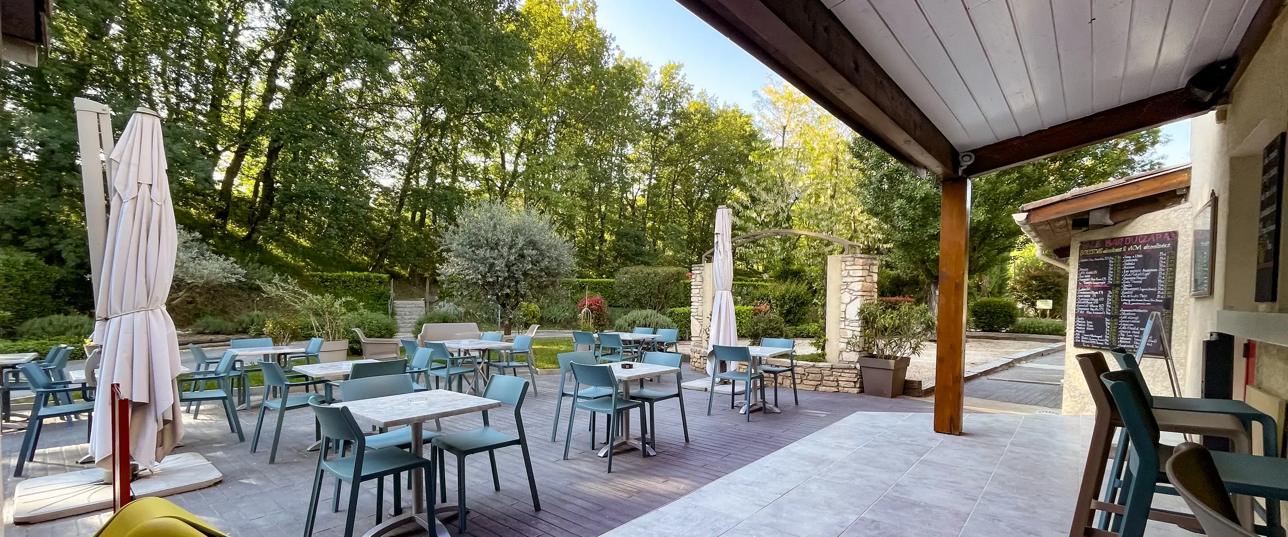 Terrasse couverte du bar-snack du Camping Le Clapas, avec ses tables ouvertes sur les arbres du camping
