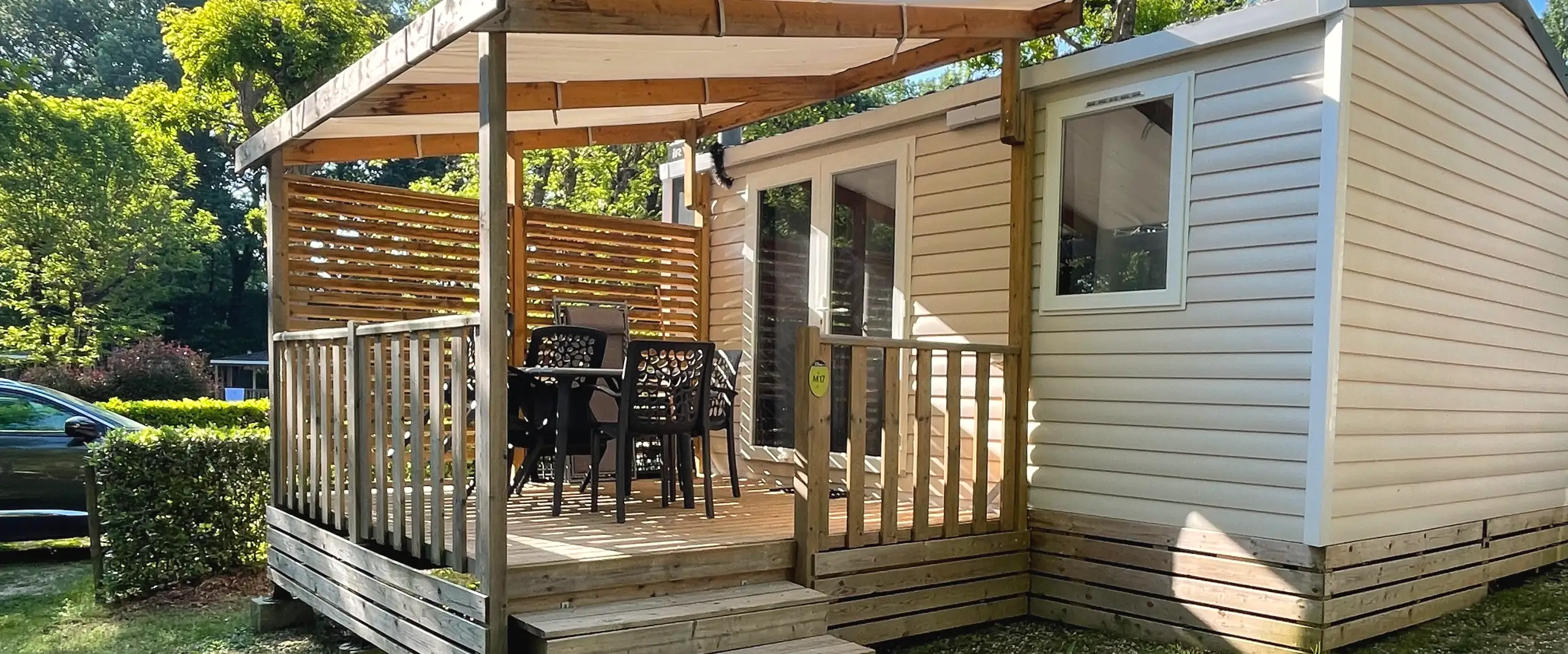 A Classic mobile home with light cladding and a covered wooden terrace, table and chairs on the lawn