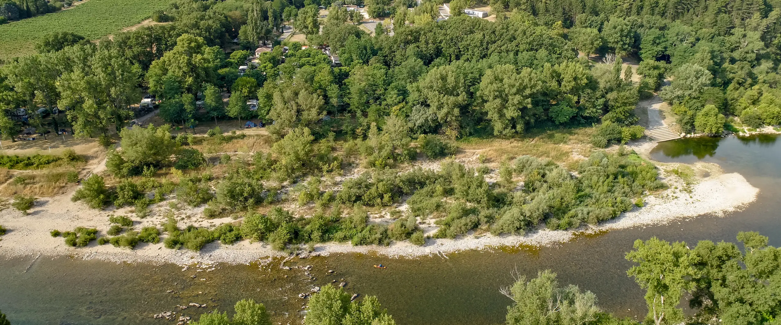 Vue aérienne de l'Ardèche, de la plage de sable et de galets au pied du camping et des kayaks sur la rivière