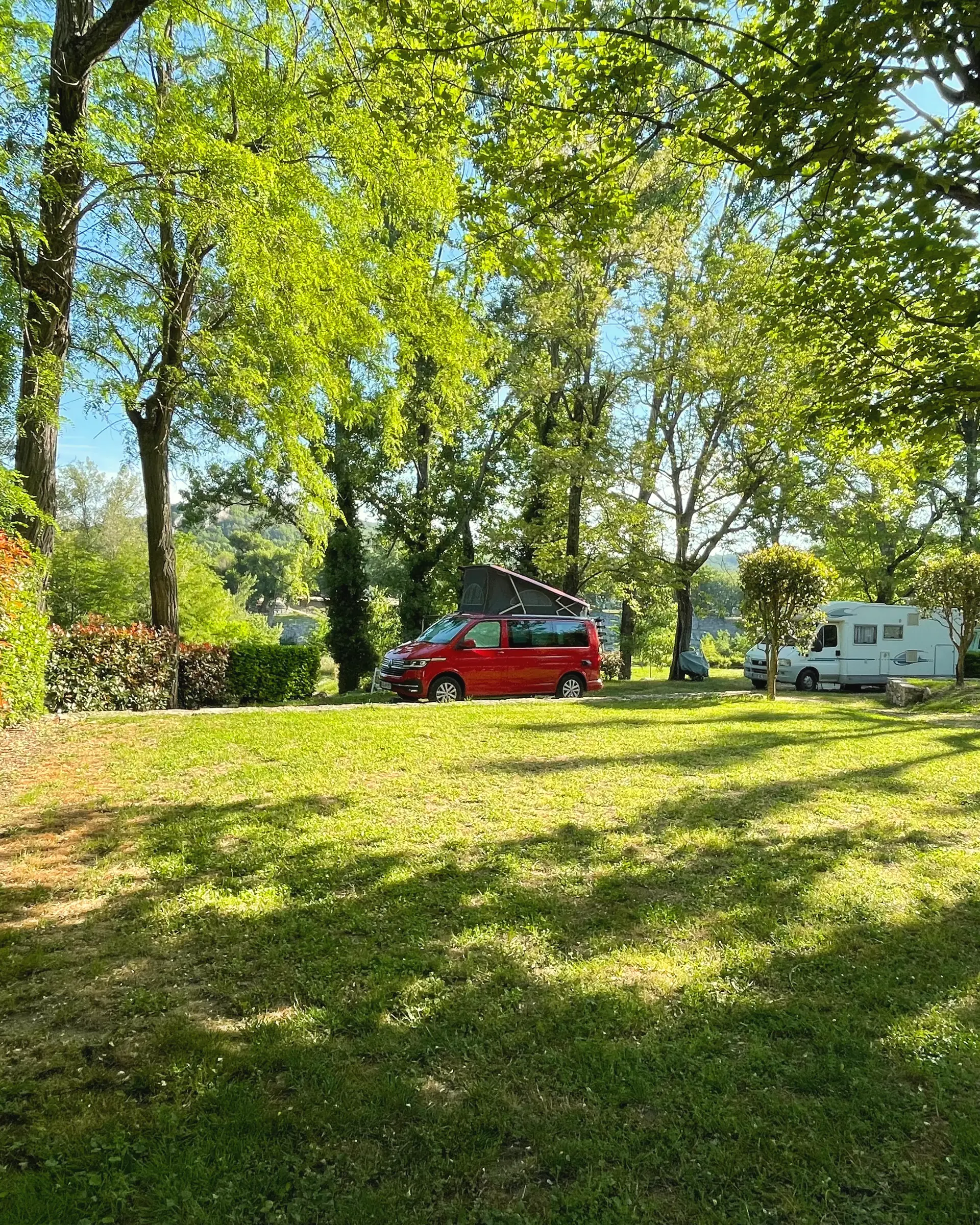 Große Rasenstellplätze im Schatten der Bäume, hinten ein Campervan