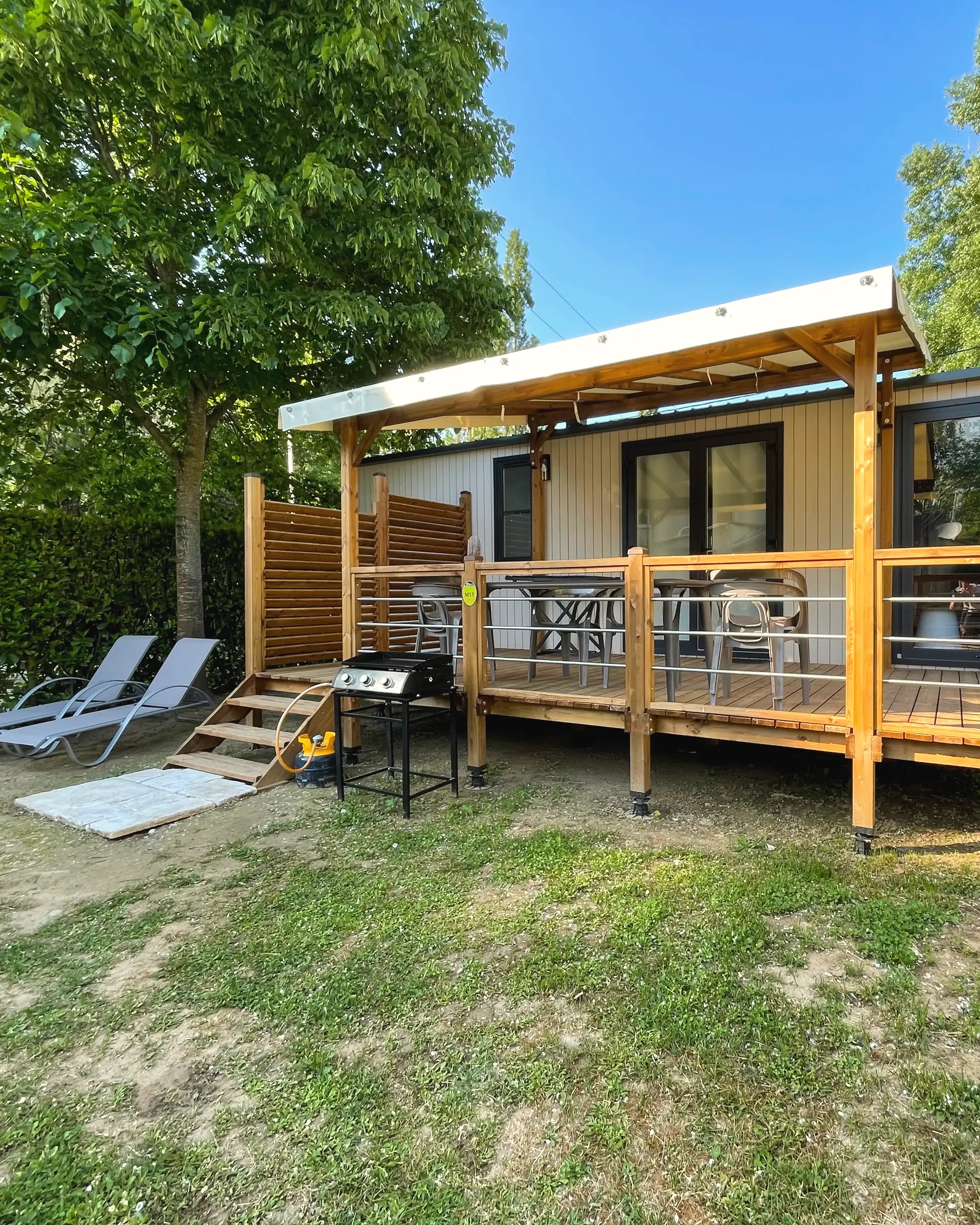 Ein Mobilheim und seine überdachte Holzterrasse, Liegestühle auf dem Rasen