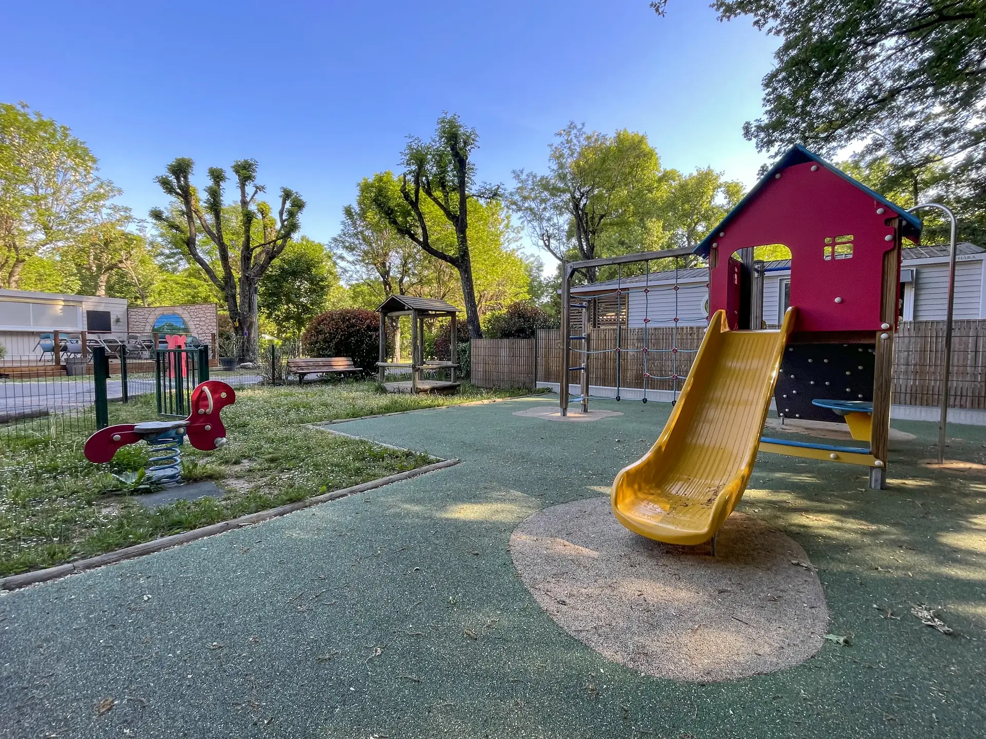 The playground's yellow slide and red playhouse, with a spring rider