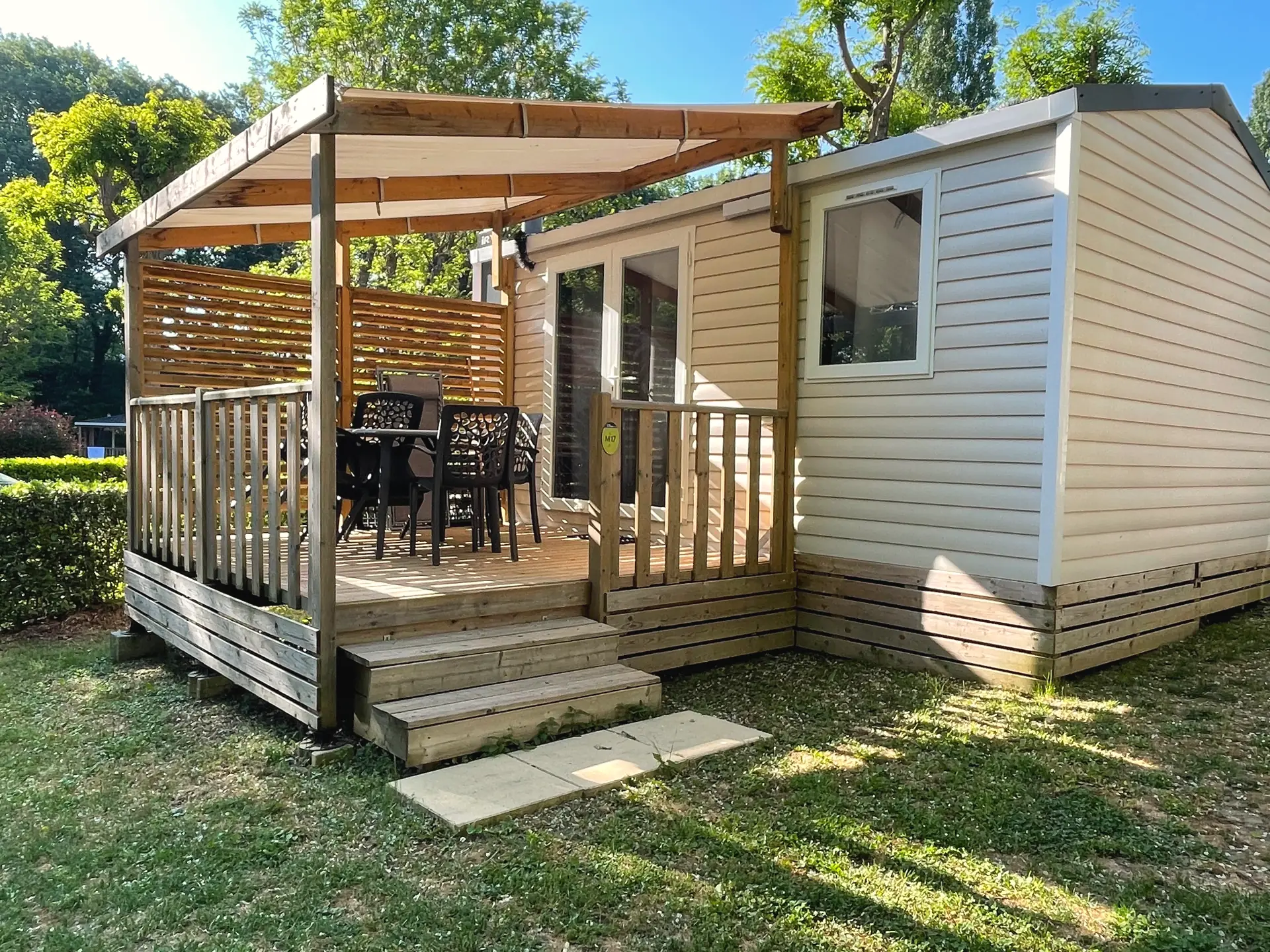 A Classic mobile home with light cladding and a covered wooden terrace, table and chairs in front of the patio door