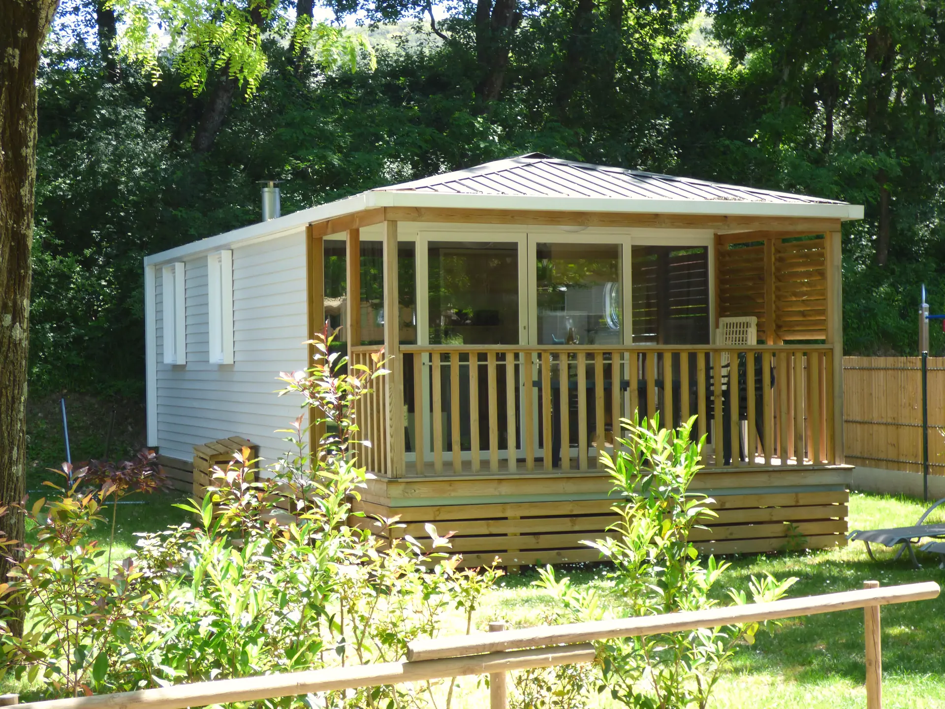 A Premium mobile home and its covered terrace with large windows, behind a flowering hedge