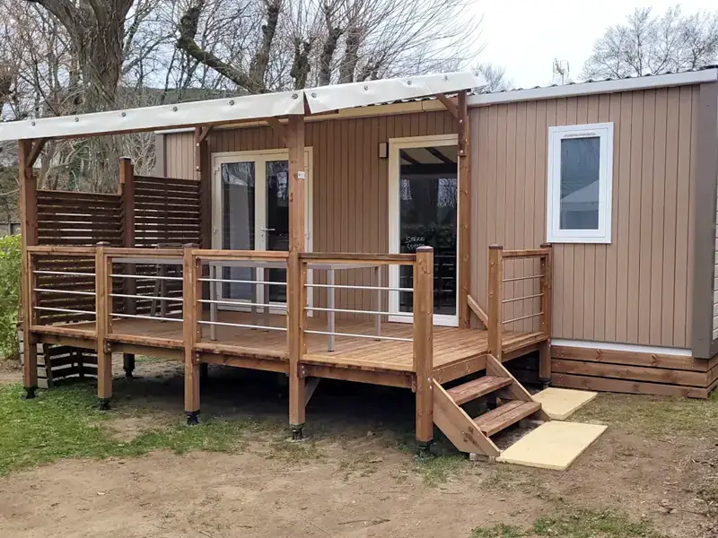 A Premium mobile home with taupe cladding and its large wooden terrace under a canopy