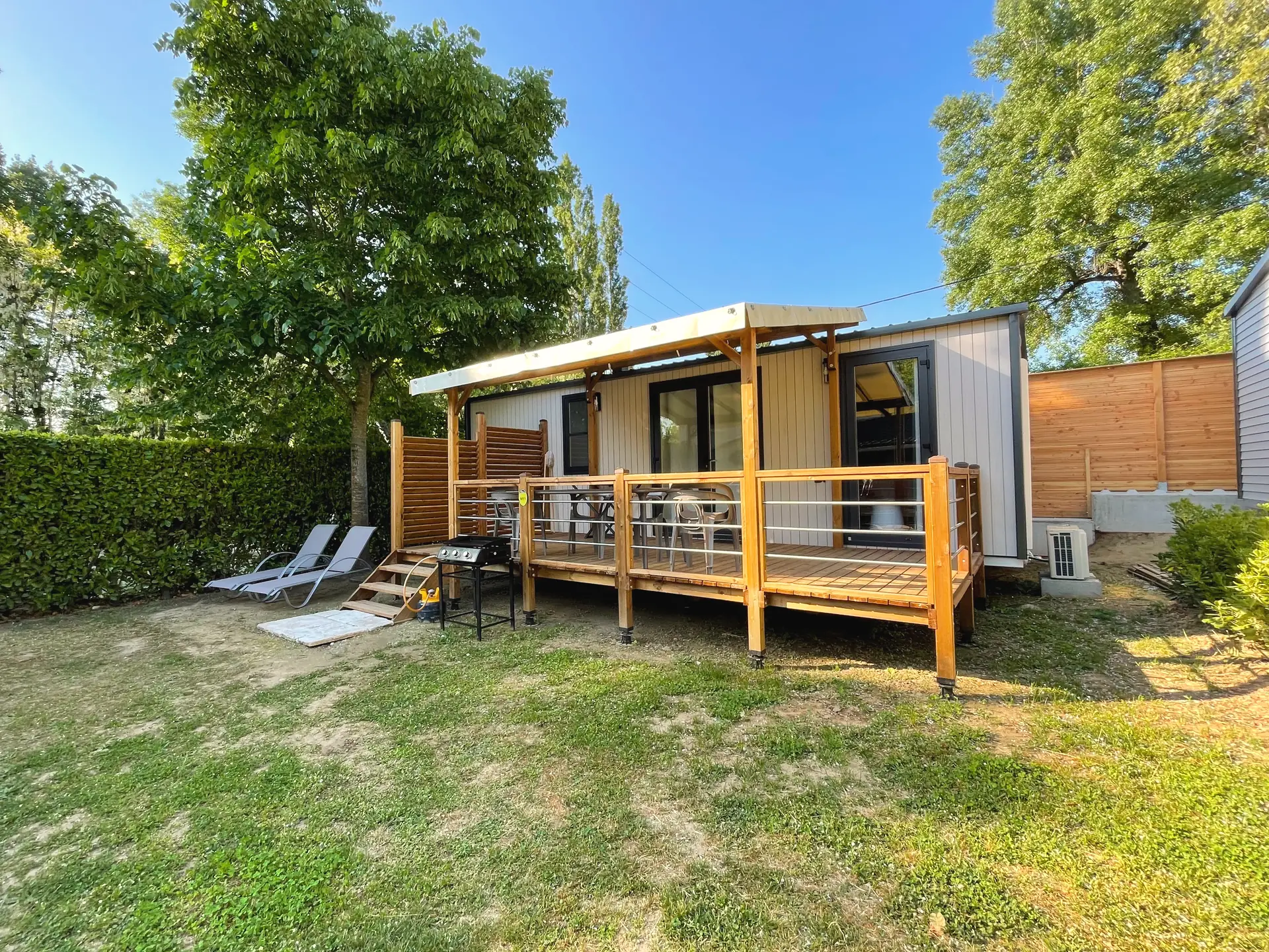 Ein Premium-Mobilheim von vorn, seine Holzterrasse und Pergola zwischen zwei Hecken