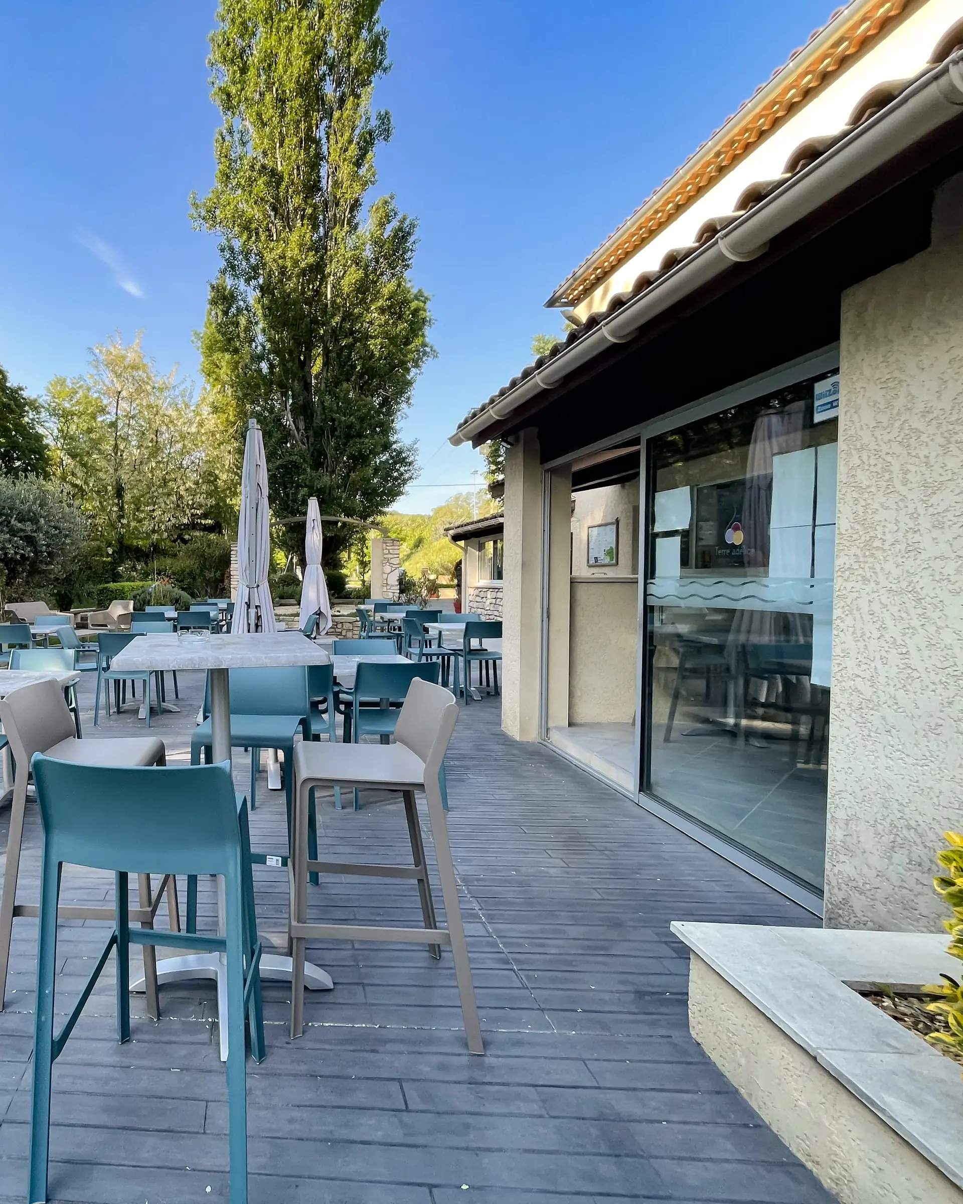 Die Terrasse vor Bar und Laden, mit Stehtischen und Stühlen vor den großen Fenstern