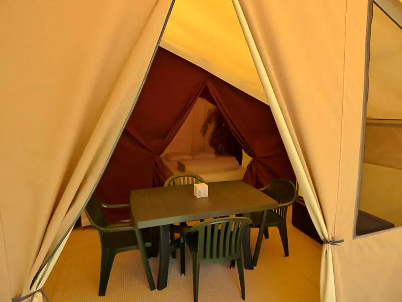 Intérieur de la tente Lodge avec table et quatre chaises, et une chambre avec grand lit en arrière-plan