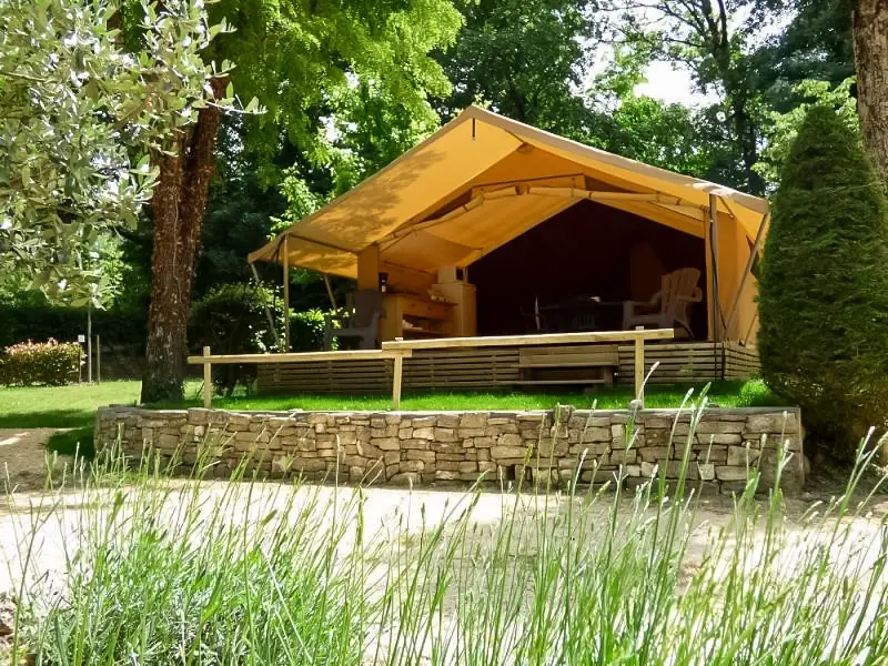 Tente Lodge ouverte sur sa terrasse en bois, derrière un muret en pierres bordé de lavande