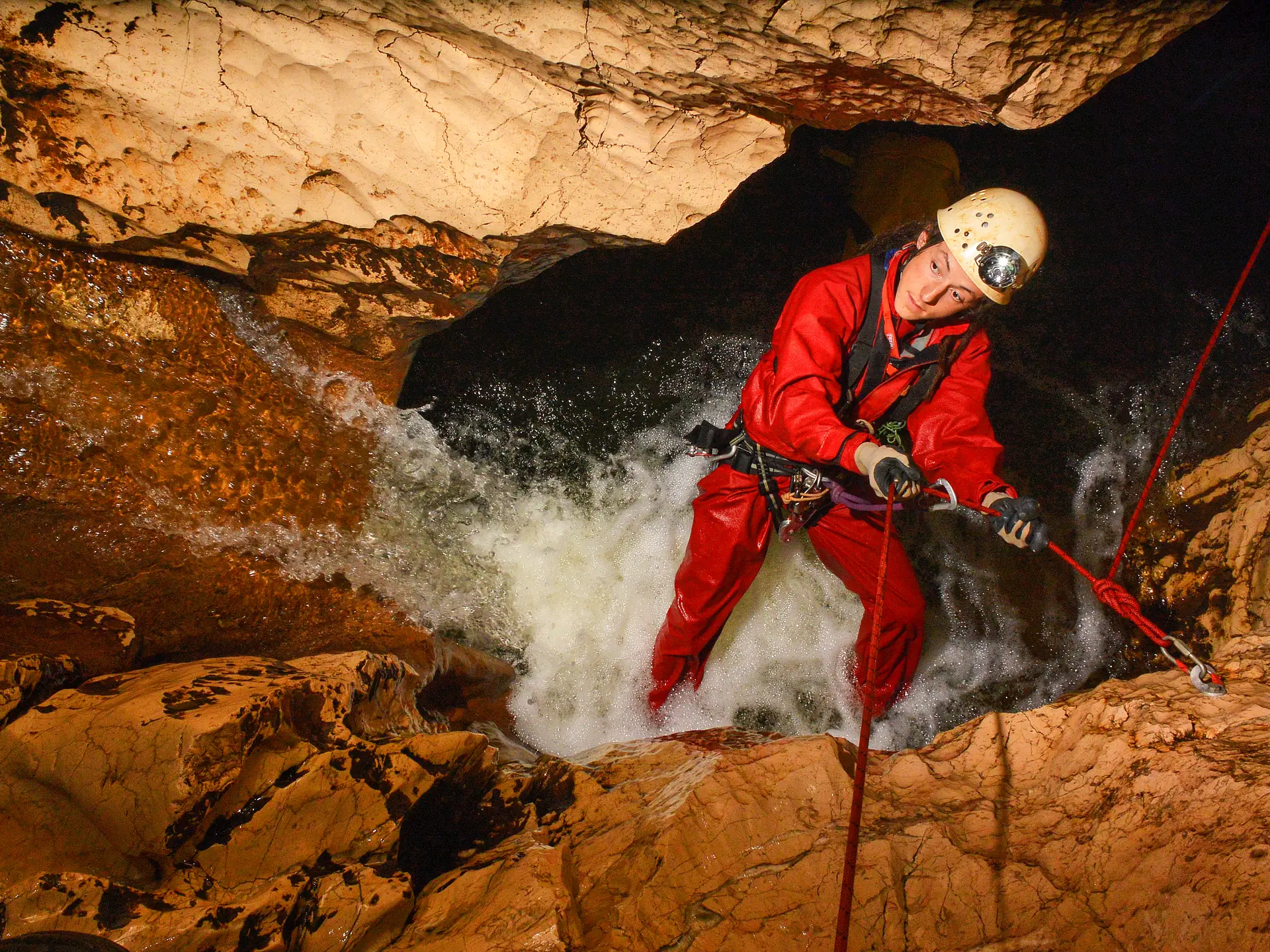 Ein Höhlenforscher im roten Overall seilt sich an einem unterirdischen Wasserfall ab